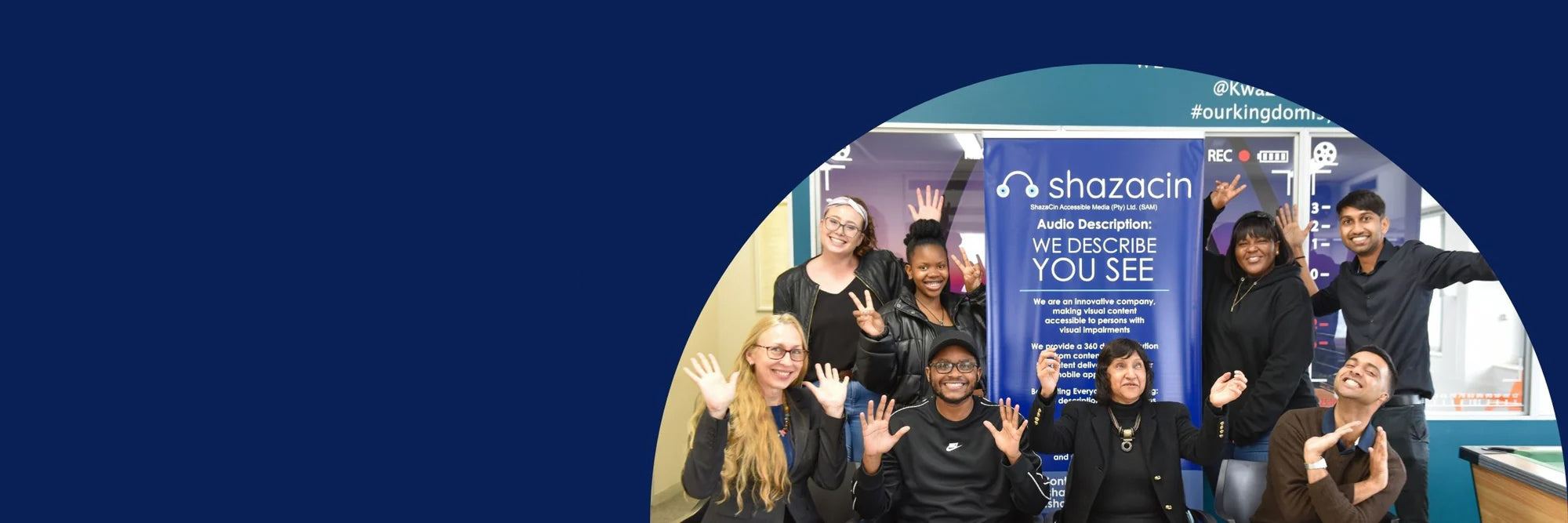 Shazacin team posing in front of a Shazacin branded backdrop with a blue gradient.